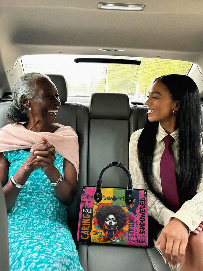 Two women sitting in a car with a colorful handbag featuring text.