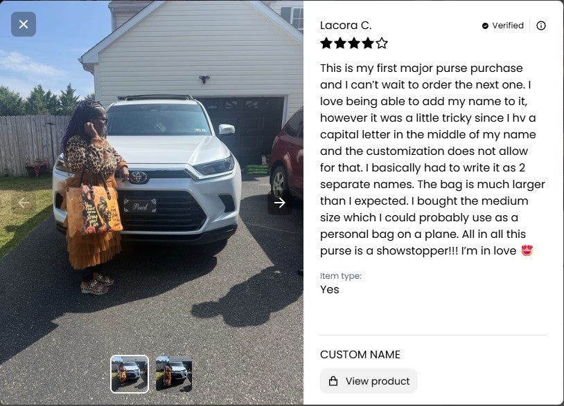 Person holding a large bag with text on it, standing next to a white car in front of a house.